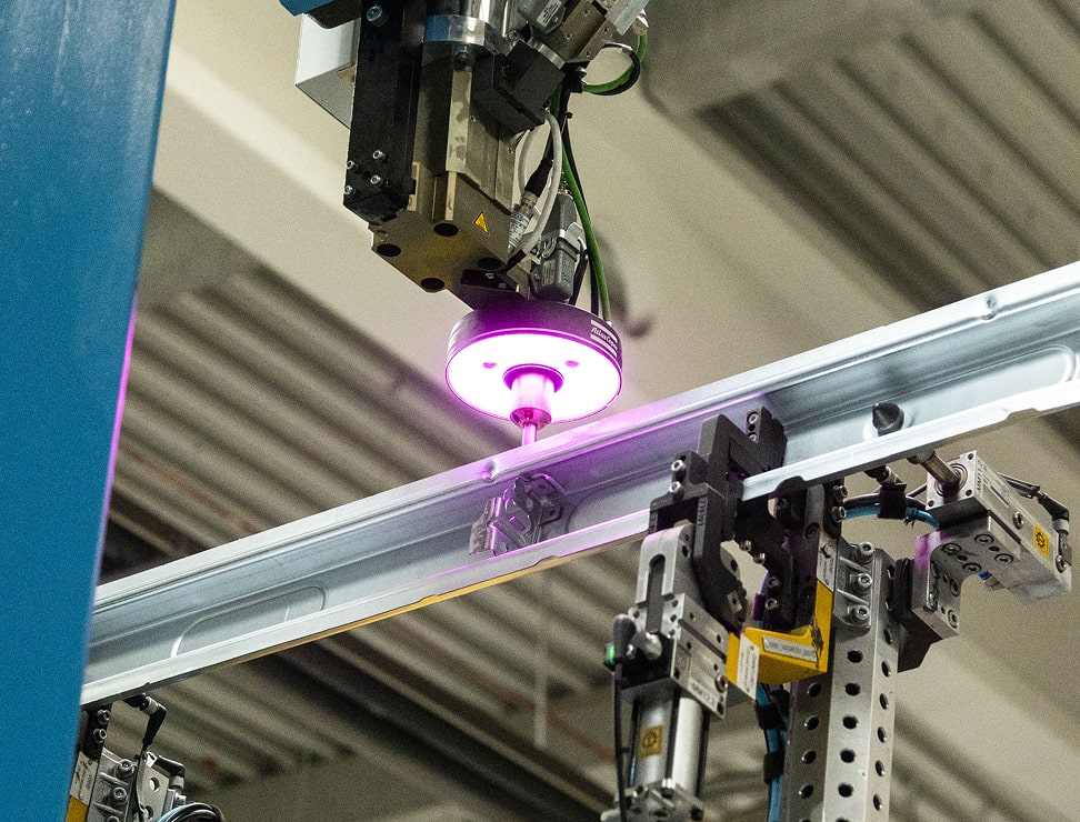 Industrieroboter mit pinkem Lichtstrahl beim präzisen Fügen eines Metallbauteils.